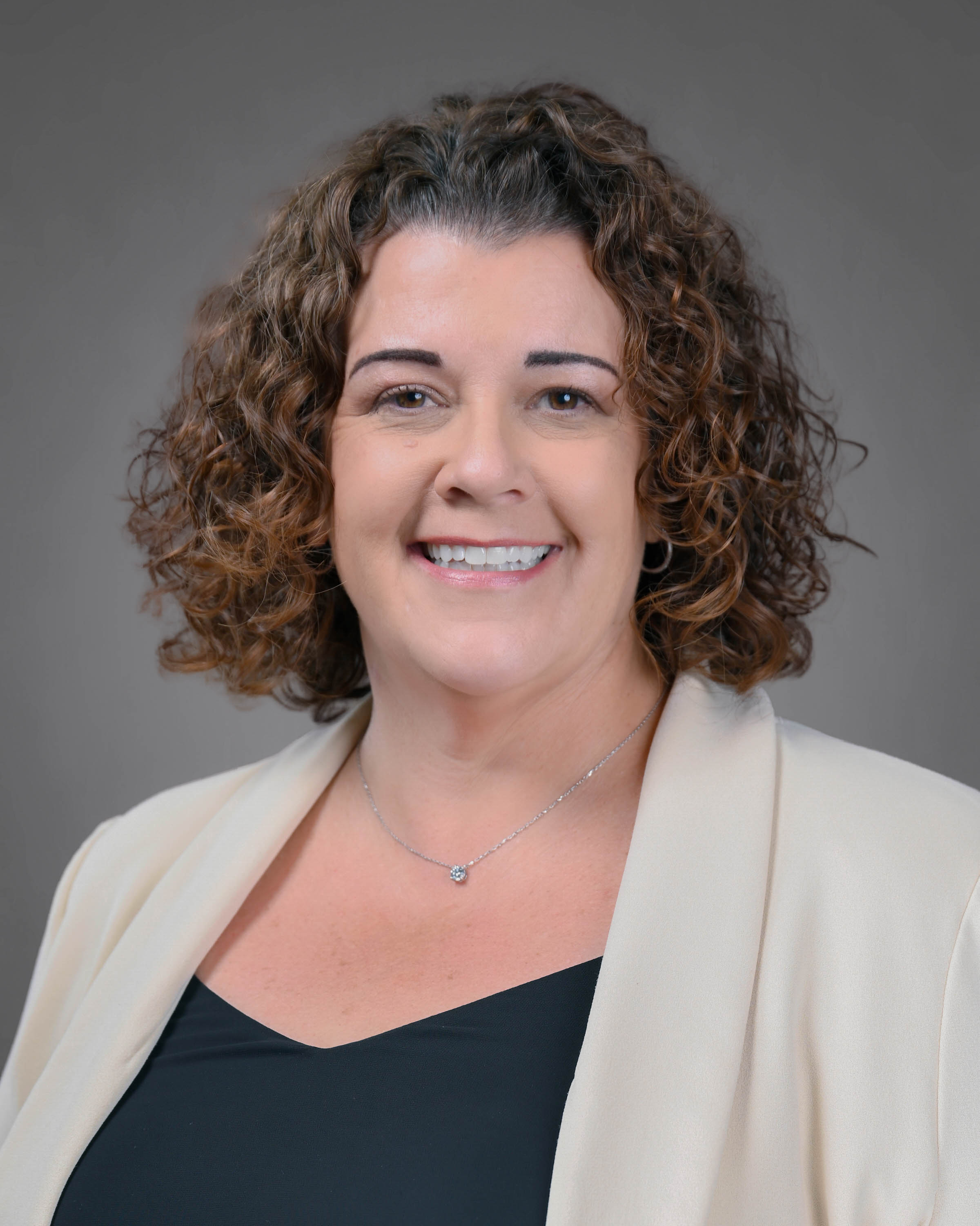 Smiling woman with curly brown hair in a white jacket with a black shirt.
